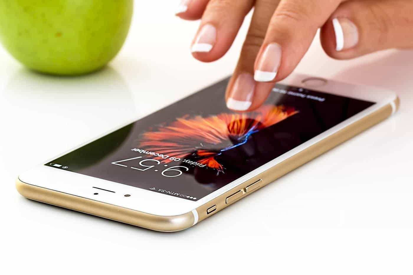 Hand tapping the screen of a smartphone on a white table