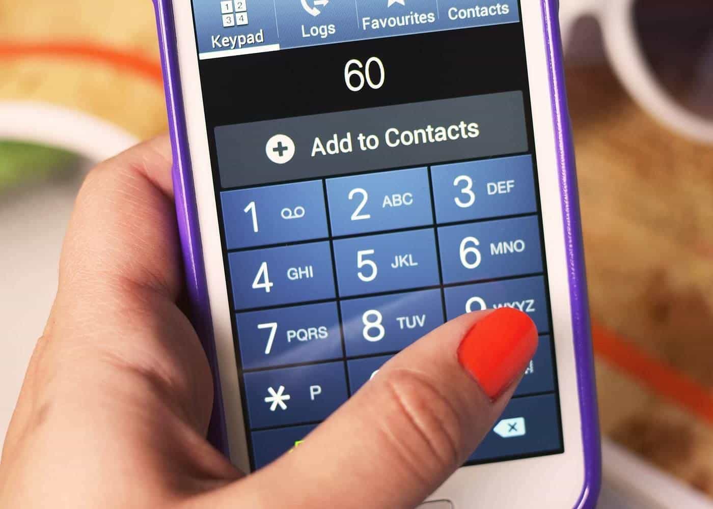 Hand holding a phone showing a dial pad with a number being entered